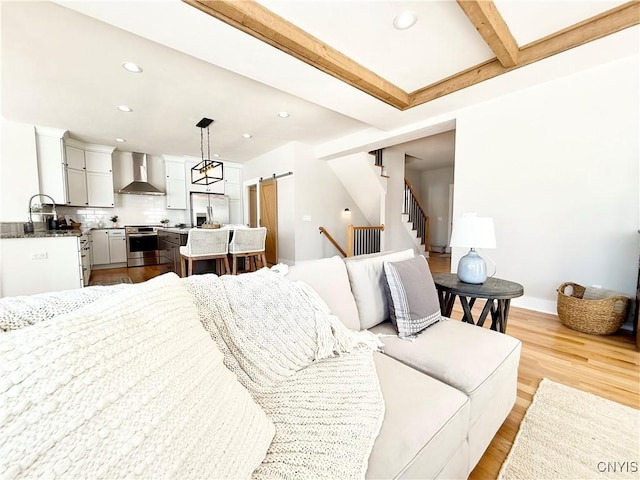 living area with a barn door, beamed ceiling, stairs, light wood-type flooring, and recessed lighting