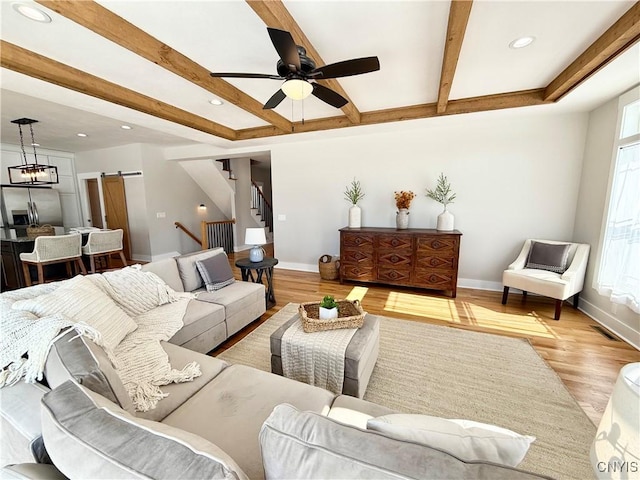 living area featuring a barn door, beamed ceiling, light wood-type flooring, and baseboards