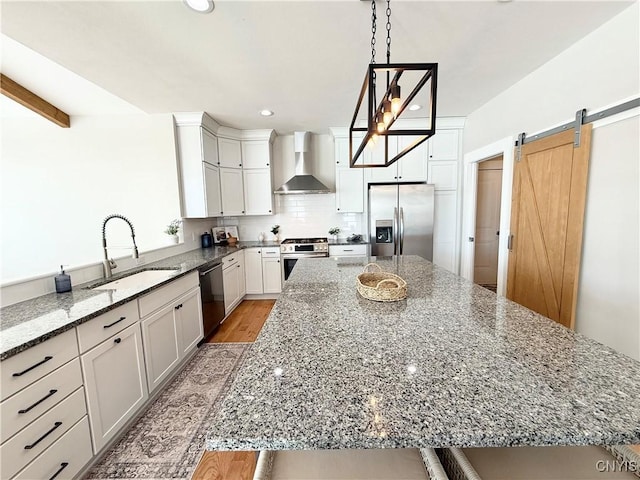 kitchen featuring appliances with stainless steel finishes, white cabinetry, a kitchen island, light stone countertops, and wall chimney exhaust hood