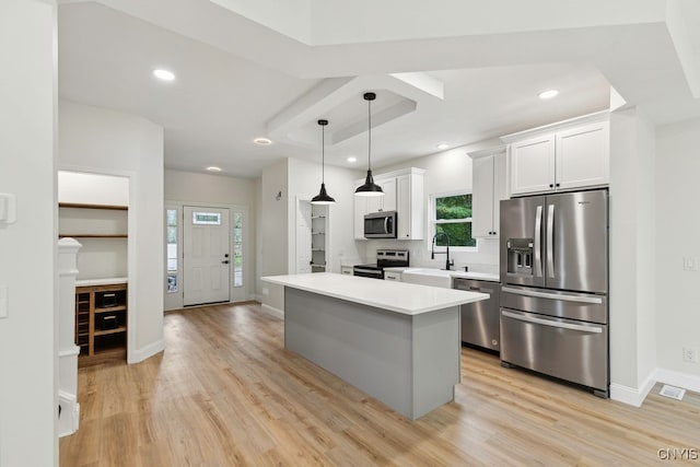 kitchen featuring appliances with stainless steel finishes, light hardwood / wood-style floors, white cabinets, pendant lighting, and a center island