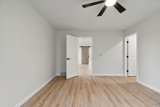 spare room featuring a barn door, ceiling fan, and light hardwood / wood-style flooring