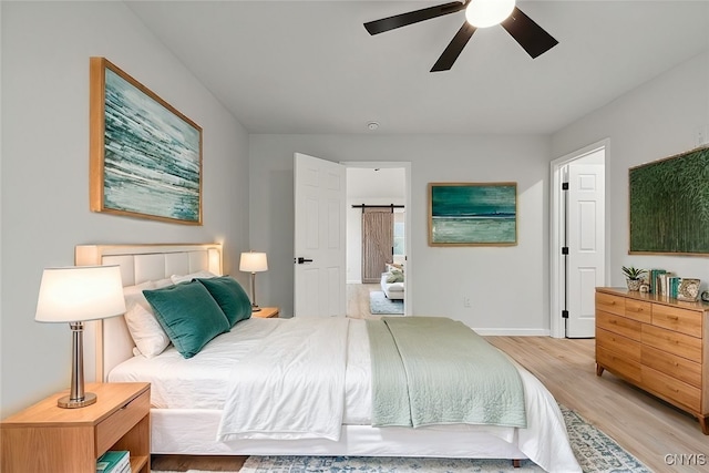 bedroom with ceiling fan, light hardwood / wood-style flooring, and a barn door