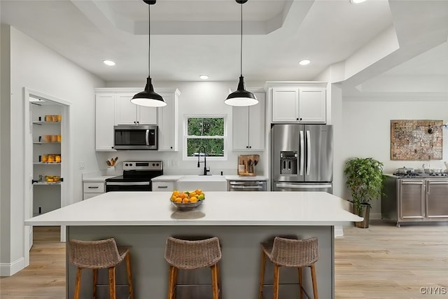 kitchen with sink, white cabinetry, stainless steel appliances, a tray ceiling, and a breakfast bar