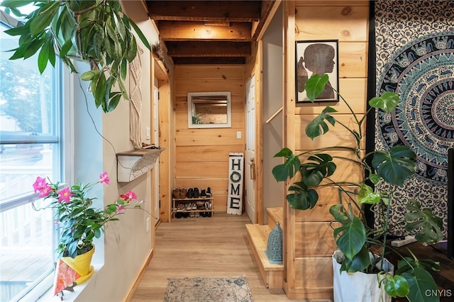 hallway with beam ceiling, light wood-type flooring, and wood walls