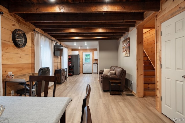 dining room featuring wooden walls, light hardwood / wood-style flooring, and beam ceiling