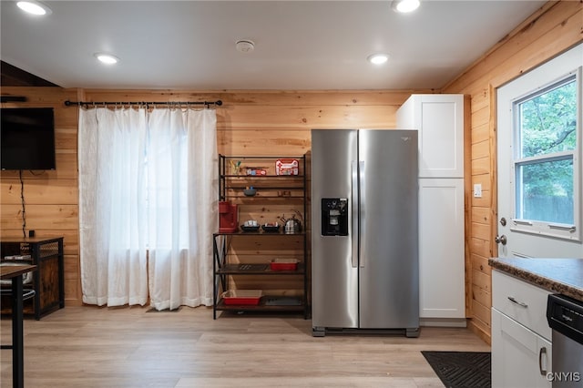 kitchen with white cabinets, wooden walls, stainless steel appliances, light stone countertops, and light hardwood / wood-style floors