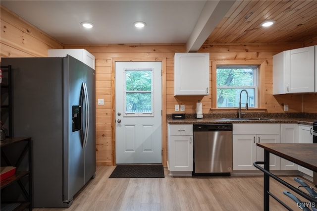 kitchen featuring white cabinets, sink, wooden walls, stainless steel appliances, and light wood-type flooring