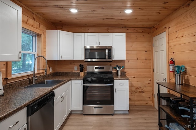 kitchen with white cabinets, wood walls, sink, light hardwood / wood-style flooring, and stainless steel appliances