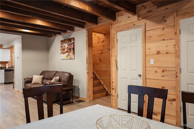 dining room featuring light wood-type flooring, wood walls, and beam ceiling