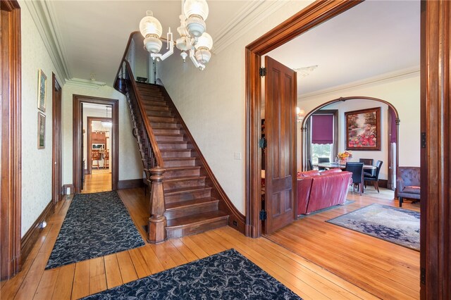 staircase with an inviting chandelier, hardwood / wood-style flooring, and ornamental molding