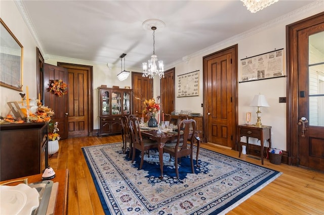 dining room with crown molding, light wood-style flooring, and a notable chandelier