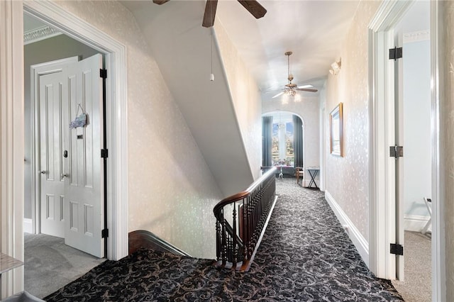 hall featuring baseboards, wallpapered walls, arched walkways, and carpet floors
