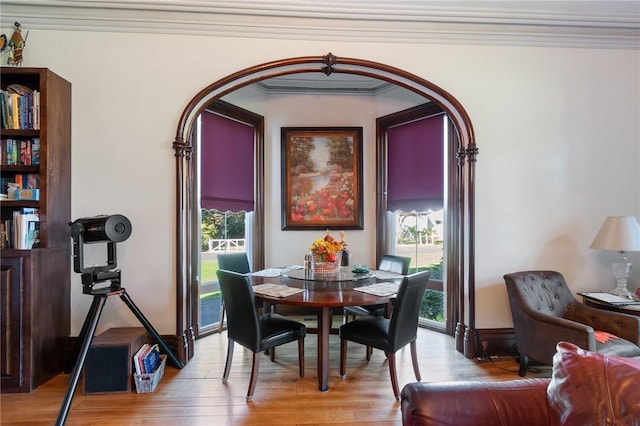 dining room featuring arched walkways, a wealth of natural light, light wood-style floors, and ornamental molding