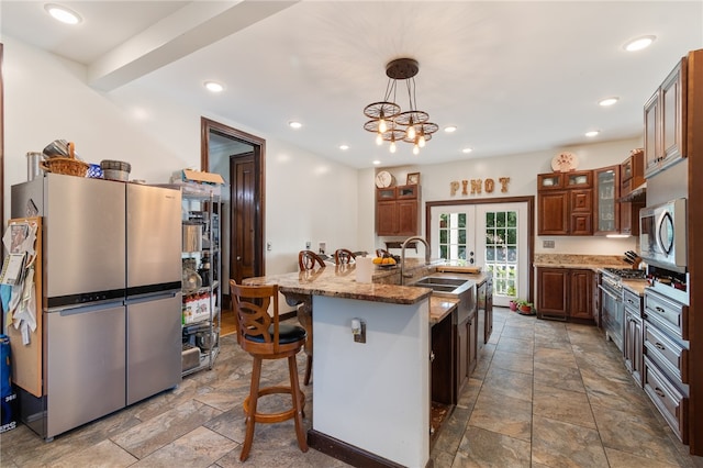 kitchen featuring appliances with stainless steel finishes, light stone countertops, a kitchen bar, a center island with sink, and sink