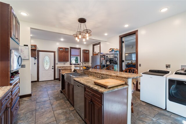 kitchen featuring washer and dryer, a kitchen bar, hanging light fixtures, stainless steel appliances, and a center island with sink