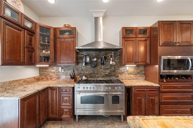 kitchen featuring wall chimney range hood, light stone counters, backsplash, and appliances with stainless steel finishes