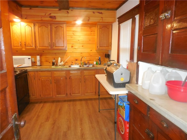 kitchen featuring light wood-type flooring, black range, wood walls, and sink