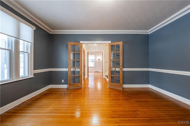 empty room with ornamental molding, wood-type flooring, and french doors