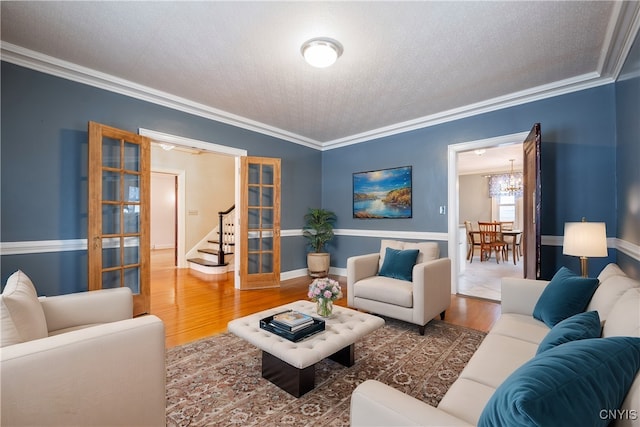 living room with a notable chandelier, wood-type flooring, french doors, a textured ceiling, and ornamental molding