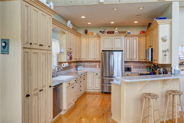 kitchen featuring appliances with stainless steel finishes, backsplash, a kitchen bar, light hardwood / wood-style flooring, and sink