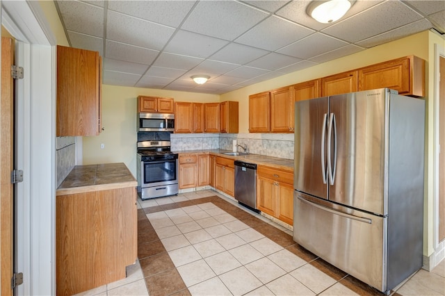 kitchen with light tile patterned flooring, sink, tasteful backsplash, a paneled ceiling, and appliances with stainless steel finishes