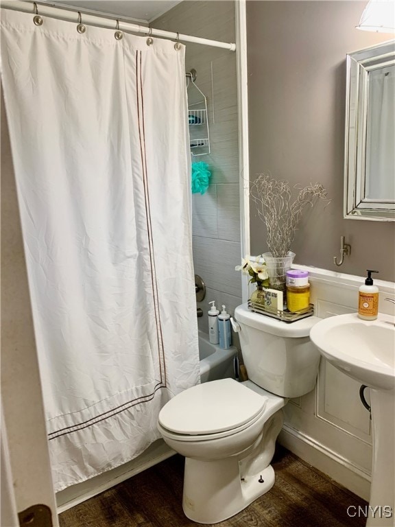 bathroom with hardwood / wood-style floors, shower / bathtub combination with curtain, and toilet