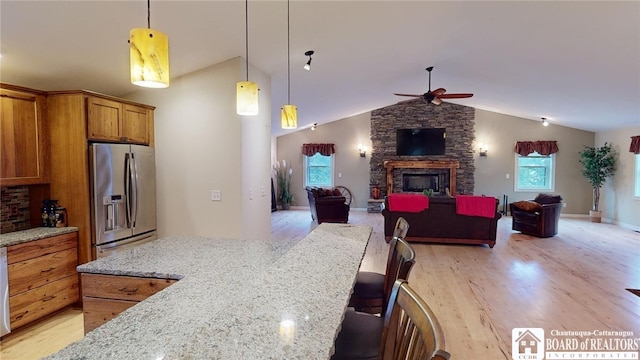 kitchen featuring stainless steel fridge, light hardwood / wood-style flooring, a fireplace, light stone countertops, and vaulted ceiling