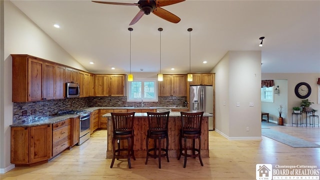 kitchen featuring pendant lighting, light wood-type flooring, a kitchen island, decorative backsplash, and appliances with stainless steel finishes