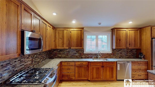 kitchen with light stone countertops, stainless steel appliances, sink, and light hardwood / wood-style flooring