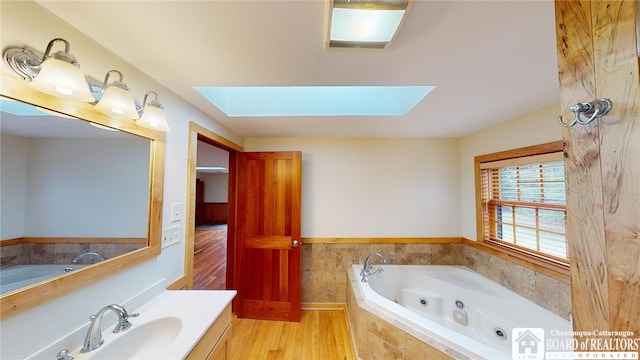 bathroom with wood-type flooring, tiled bath, vanity, and a skylight