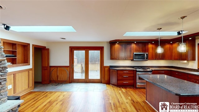 kitchen featuring stainless steel appliances, light hardwood / wood-style flooring, a skylight, decorative light fixtures, and dark stone counters