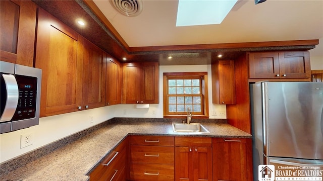 kitchen with dark stone countertops, sink, a skylight, and stainless steel appliances