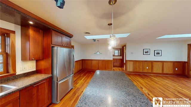 kitchen with a skylight, hanging light fixtures, sink, light hardwood / wood-style flooring, and stainless steel refrigerator