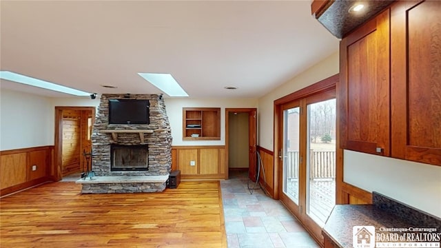 unfurnished living room with a skylight, a fireplace, light wood-type flooring, and wood walls