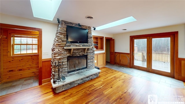 living room with light hardwood / wood-style floors, a skylight, wood walls, and a fireplace