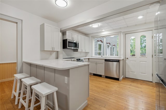 kitchen featuring light hardwood / wood-style floors, white cabinetry, kitchen peninsula, a kitchen breakfast bar, and stainless steel appliances