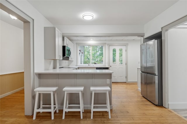 kitchen featuring a breakfast bar area, stainless steel appliances, kitchen peninsula, and light hardwood / wood-style flooring