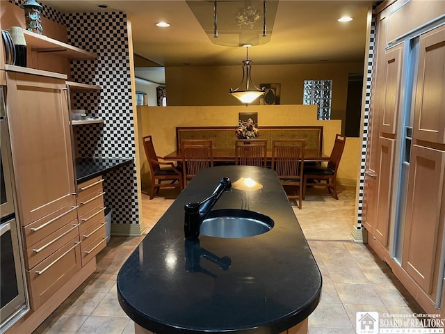 kitchen with dark stone countertops, pendant lighting, sink, and oven