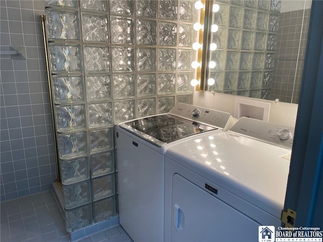 clothes washing area with tile walls, tile patterned floors, and washer and clothes dryer