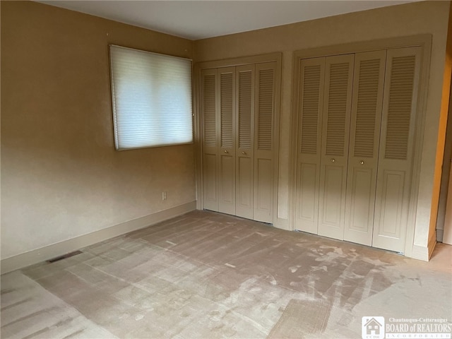 unfurnished bedroom with two closets and light colored carpet