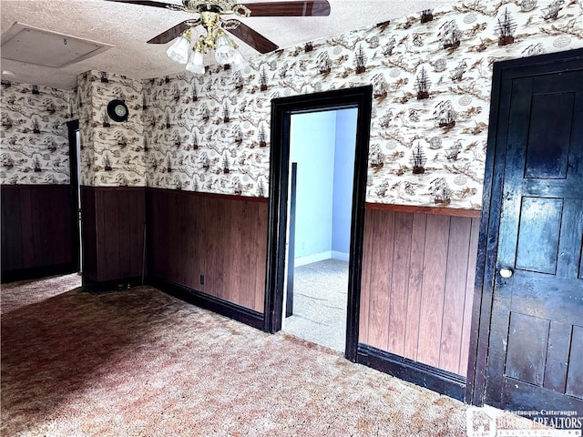 carpeted spare room featuring wooden walls, a textured ceiling, and ceiling fan