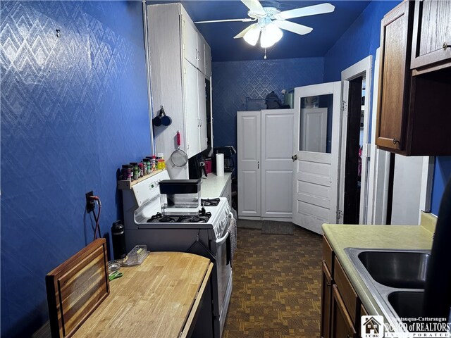 kitchen with white gas stove, sink, ceiling fan, dark brown cabinetry, and dark parquet floors