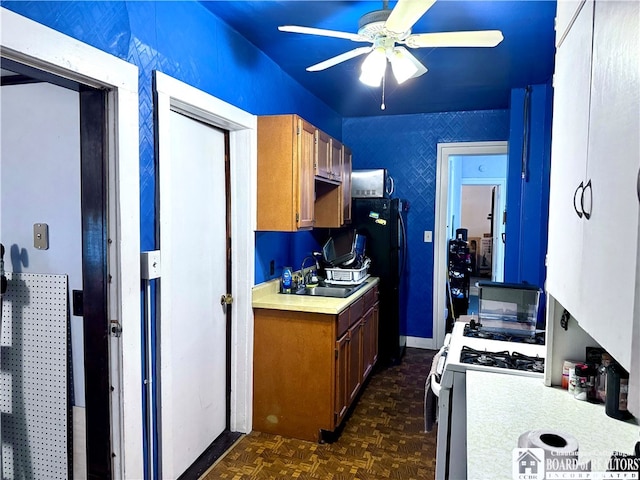 kitchen featuring black fridge, sink, white gas range, ceiling fan, and dark parquet flooring