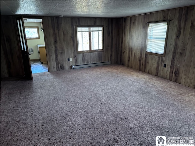 carpeted spare room with a baseboard heating unit, wood walls, and a wealth of natural light