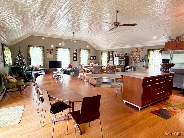 dining area with ceiling fan, ornamental molding, light wood-type flooring, and vaulted ceiling