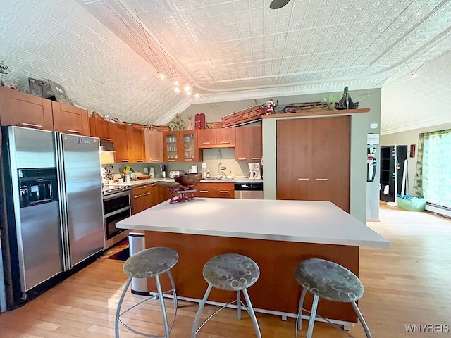 kitchen featuring vaulted ceiling, a kitchen island, stainless steel appliances, a kitchen bar, and light hardwood / wood-style flooring