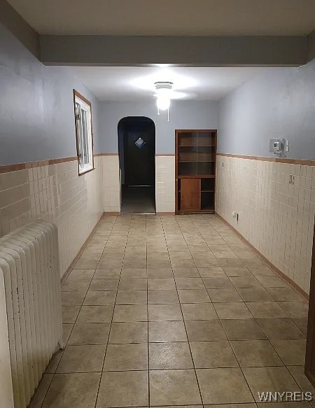 corridor with light tile patterned floors, beamed ceiling, tile walls, and radiator heating unit