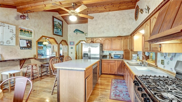 kitchen with stainless steel appliances, sink, high vaulted ceiling, a center island, and light hardwood / wood-style floors