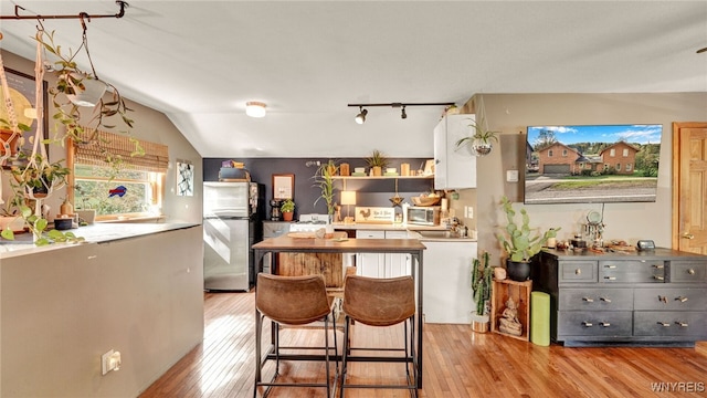 kitchen with light hardwood / wood-style flooring, white cabinetry, stainless steel appliances, and vaulted ceiling