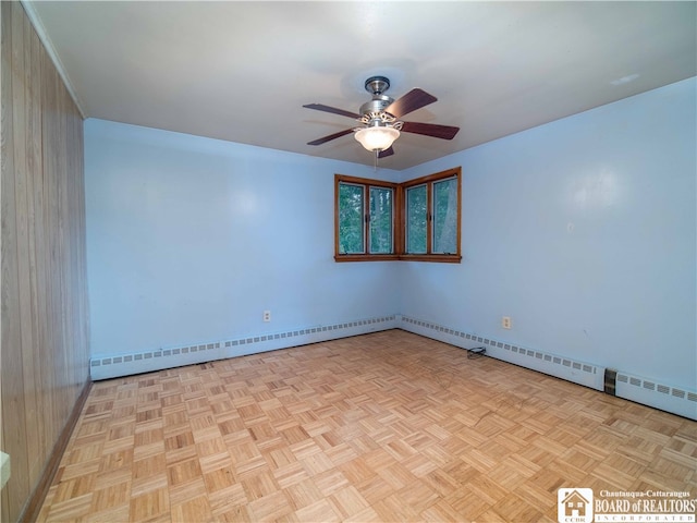 empty room with light parquet floors, wooden walls, ceiling fan, and a baseboard radiator